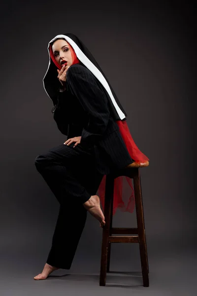 Pieds nus nonne sexy à la mode posant en costume noir et écharpe rouge, sur gris — Photo de stock