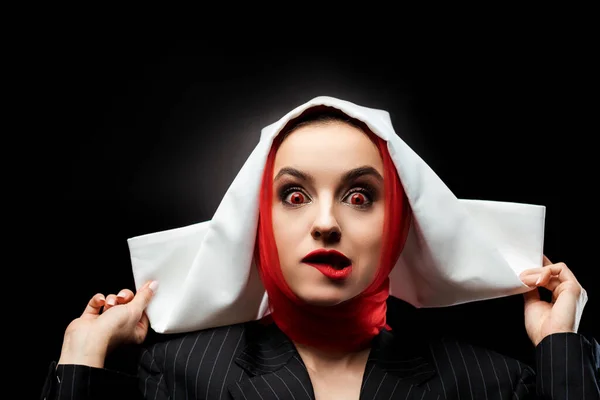 Attractive sexy demonic nun with red eyes biting lip isolated on black — Stock Photo