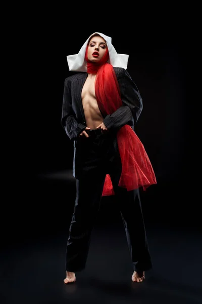 Attractive fashionable sexy nun posing in black suit and red scarf, on black — Stock Photo