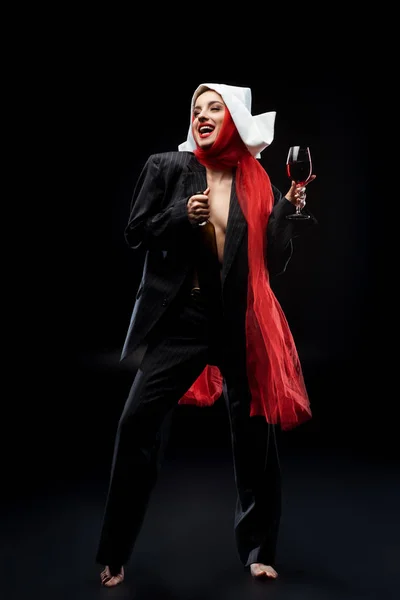 Emotional sensual barefoot nun holding glass and bottle of red wine on black — Stock Photo