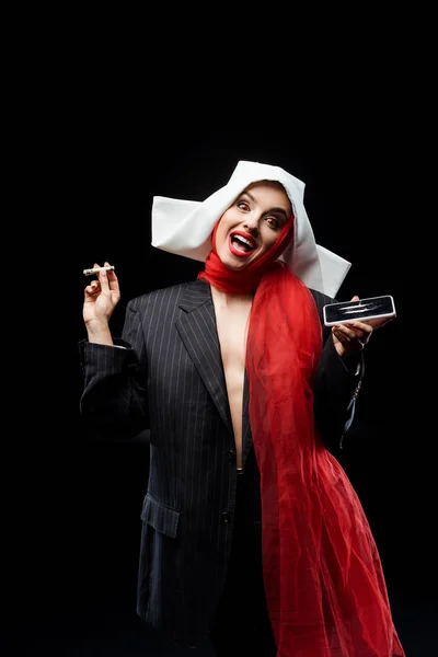 Emotional sexy demonic nun holding dollar banknote and smartphone with cocaine lines isolated on black — Stock Photo