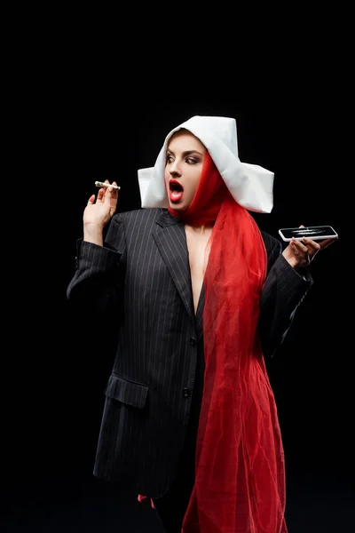 Shocked sexy demonic nun holding dollar banknote and smartphone with cocaine lines isolated on black — Stock Photo