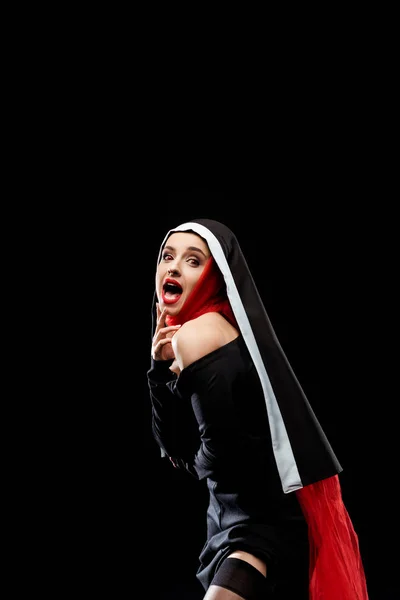 Choqué nonne sexy posant en robe noire, bas et écharpe rouge, isolé sur noir — Photo de stock