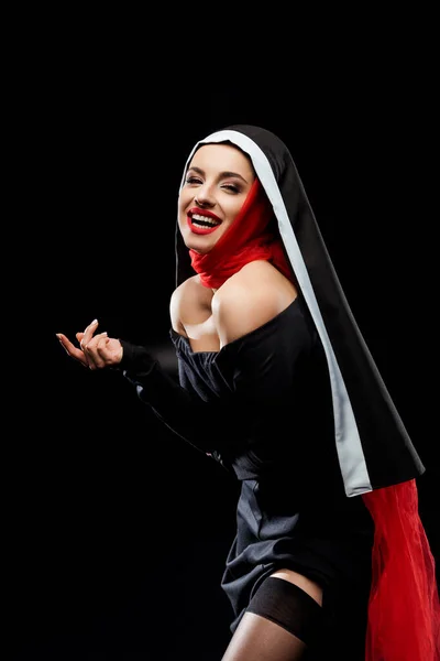 Belle nonne sexy riant et posant en robe noire et écharpe rouge, isolé sur noir — Photo de stock