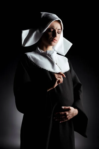 Беспокойная беременная монахиня держит крест и трогает живот на серой — стоковое фото