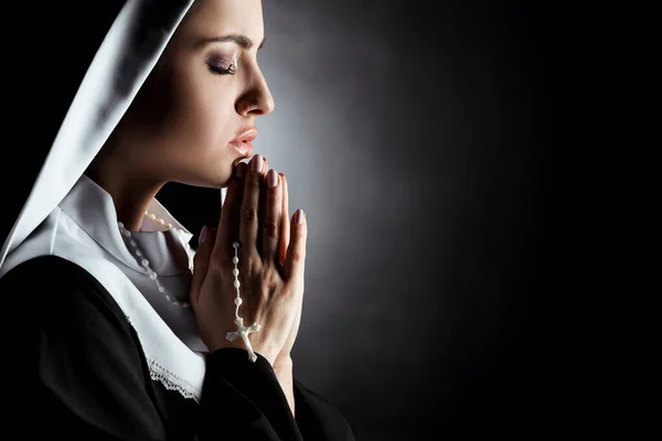 Schöne junge Nonne mit geschlossenen Augen, die mit Kreuz auf grau betet — Stockfoto