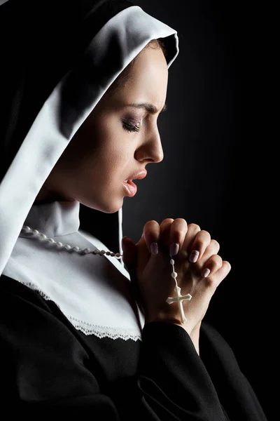 Beautiful worried nun praying with cross isolated on black — Stock Photo