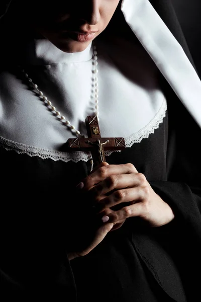 Vista recortada de monja joven sosteniendo cruz aislada en negro - foto de stock