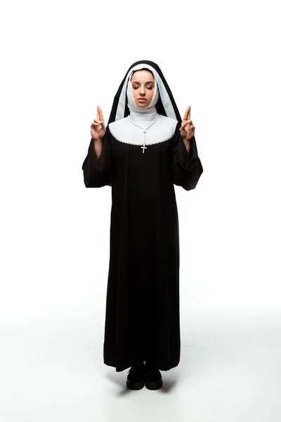 Beautiful nun with closed eyes holding fingers crossed, isolated on white — Stock Photo