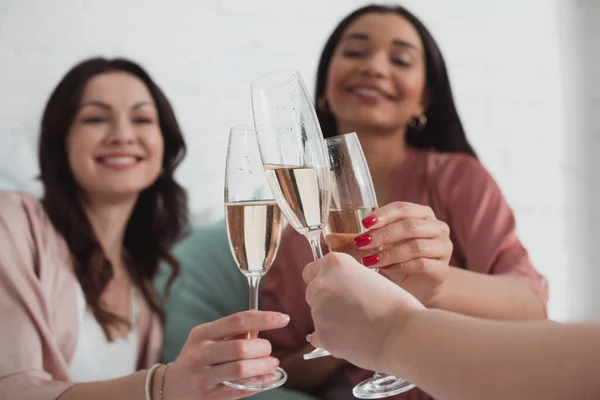 Vista cortada de mulheres africanas americanas e caucasianas sorrindo e clinking com taças de champanhe no quarto — Fotografia de Stock