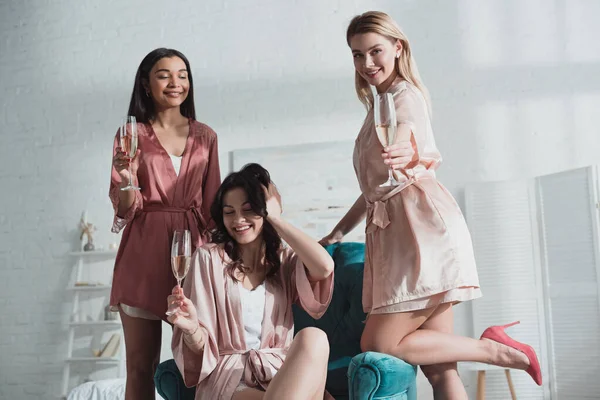 Foco seletivo de mulheres multiétnicas com taças de champanhe na despedida de solteira no quarto — Fotografia de Stock