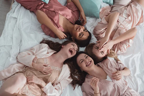 Draufsicht auf glückliche multikulturelle Frauen, die bei der Junggesellenabschiedsparty lächeln und auf dem Bett liegen — Stockfoto