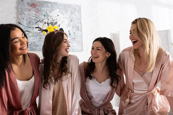 Mujeres multiétnicas riendo y mirándose en la habitación en la despedida de soltera - foto de stock