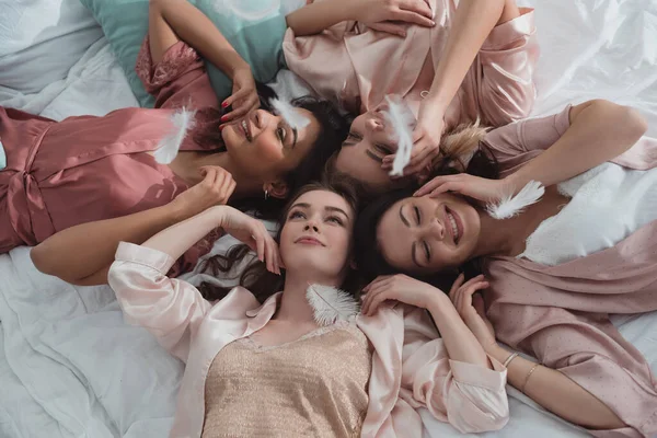 Selective focus of multicultural women resting together on bed with feathers at bachelorette party — Stock Photo
