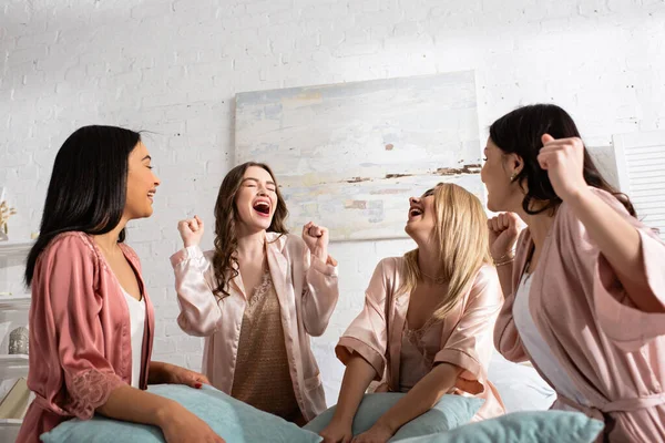 Excited multicultural friends laughing together with pillows in room at bachelorette party — Stock Photo