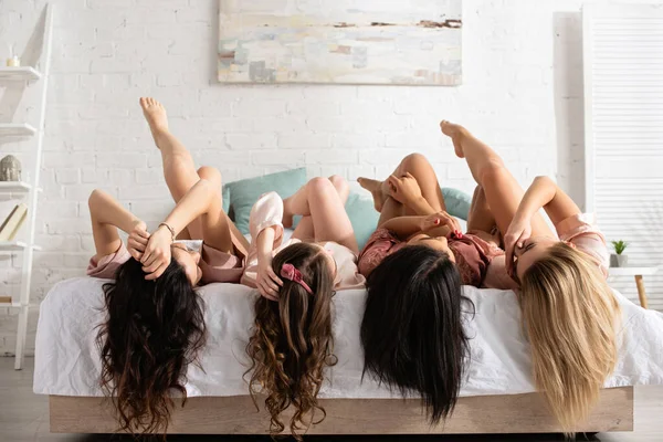 Mulheres multiculturais com pernas cruzadas deitadas na cama na despedida de solteira — Fotografia de Stock