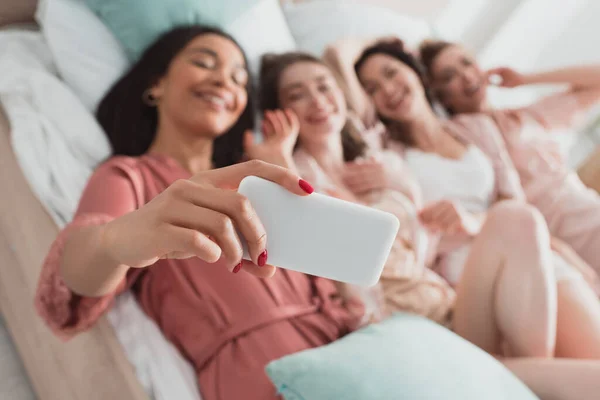 Foco seletivo da menina americana africana tomando selfie com os amigos na cama na festa de despedida de solteira — Fotografia de Stock