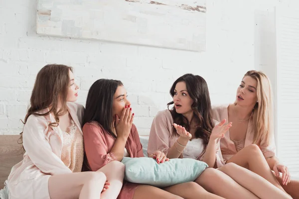 Multicultural friends talking and looking at each other on bed, at bachelorette party — Stock Photo