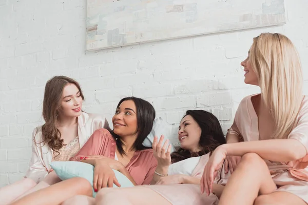 Multikulturelle Frauen sehen einander an und lächeln auf Junggesellenabschied im Bett — Stockfoto