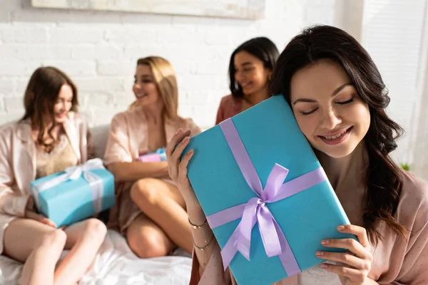 Selektiver Fokus des brünetten Mädchens mit Geschenk in der Nähe multiethnischer Freunde, die Geschenkboxen auf dem Bett bei der Junggesellenabschiedsparty halten — Stockfoto