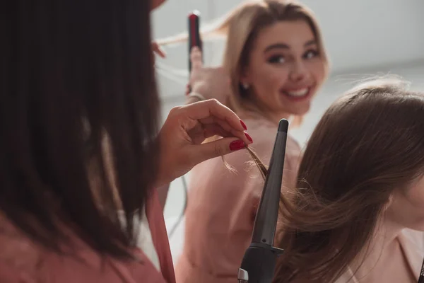 Cropped view of african american girl doing hairstyle with curling iron at bachelorette party — Stock Photo