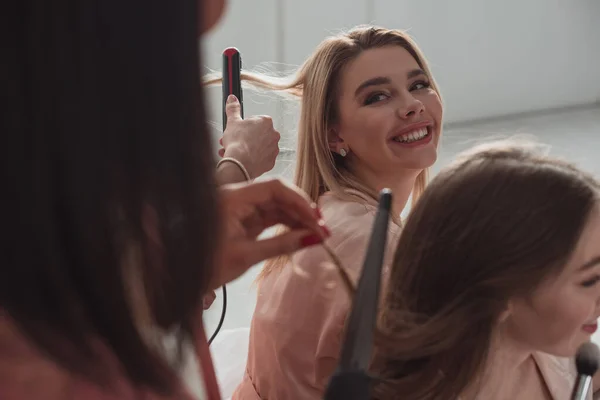 Cropped view of multicultural friends doing hairstyles with curling irons at bachelorette party — Stock Photo