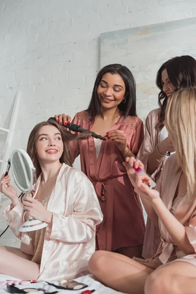 Enfoque selectivo de mujeres multiétnicas haciendo peinado, manicura y sonriendo en despedida de soltera - foto de stock