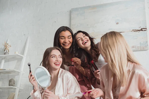 Mujeres multiétnicas haciendo peinado, manicura y riéndose en despedida de soltera - foto de stock