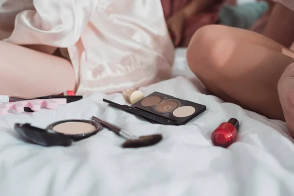 Vista cortada de mulheres perto de cosméticos na cama — Fotografia de Stock