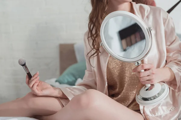 Vista ritagliata della donna con specchio e pennello cosmetico in camera — Foto stock