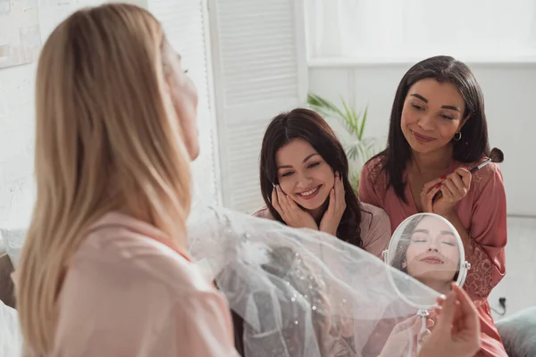 Foco seletivo de mulheres multiétnicas admirando noiva bonita na despedida de solteira no quarto — Fotografia de Stock