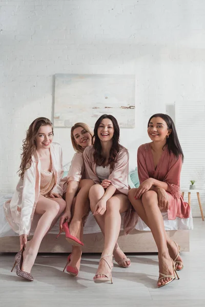 Multicultural women smiling and looking at camera on bed — Stock Photo