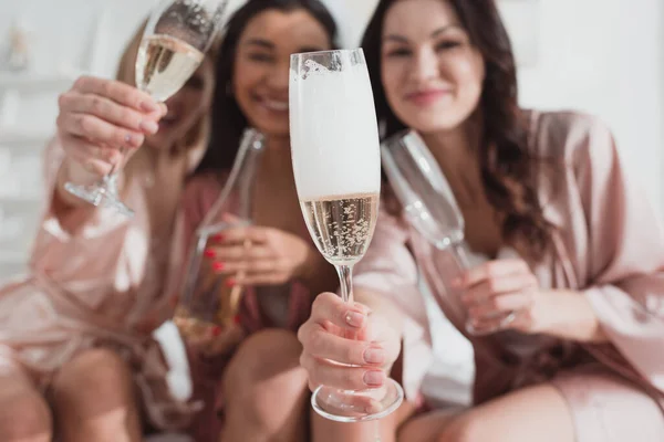 Foco seletivo de amigos multiétnicos felizes segurando copos de champanhe e olhando para a câmera na festa de despedida de solteira — Fotografia de Stock