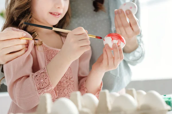 Vista recortada de niño feliz pintura huevo de Pascua cerca de la madre - foto de stock