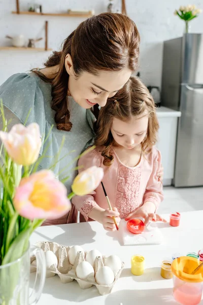 Selective focus of happy kid and mother near tulips and chicken eggs — Stock Photo