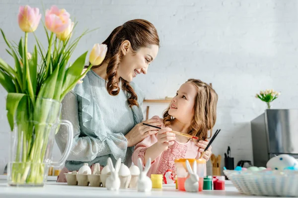 Messa a fuoco selettiva di bambino carino e madre felice guardando l'un l'altro vicino a tulipani e uova di Pasqua — Foto stock