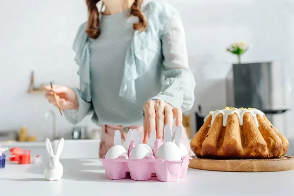 Обрезанный вид женщины, берущей куриное яйцо возле пасхального торта и декоративного кролика — стоковое фото