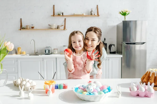 Adorable enfant et mère heureuse près des œufs de poulet, lapins décoratifs, pain de Pâques et tulipes — Photo de stock