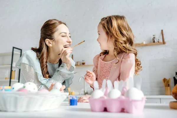 Selective focus of cheerful mother and happy daughter near painted easter eggs — Stock Photo
