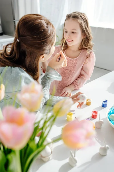 Selektiver Fokus des glücklichen Kindes auf die Mutter in der Nähe von Tulpen und dekorativen Hasen — Stockfoto