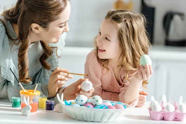 Feliz madre y linda hija pintando huevos de Pascua - foto de stock