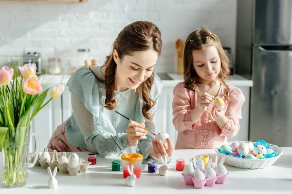 Enfoque selectivo de lindo niño y madre pintando huevos de Pascua cerca de tulipanes - foto de stock