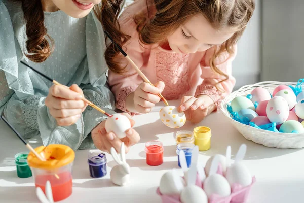 Selective focus of happy mother and cute daughter painting easter eggs near decorative bunnies — Stock Photo