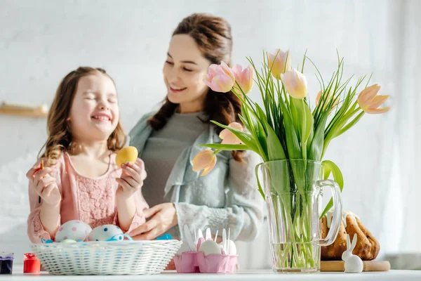 Foco seletivo de tulipas perto de ovos de galinha, pão de Páscoa, mãe feliz e filha — Fotografia de Stock