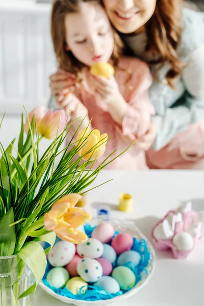 Foco seletivo de tulipas perto de mãe feliz e bonito filha pintura ovo de Páscoa — Fotografia de Stock