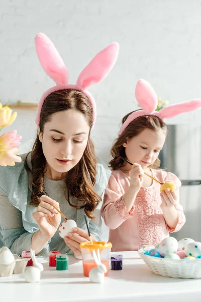 Selective focus of mother and kid in bunny ears painting chicken eggs — Stock Photo