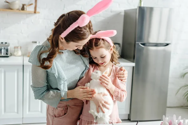 Мать обнимает ребенка в кроличьи уши с игрушечным кроликом — стоковое фото