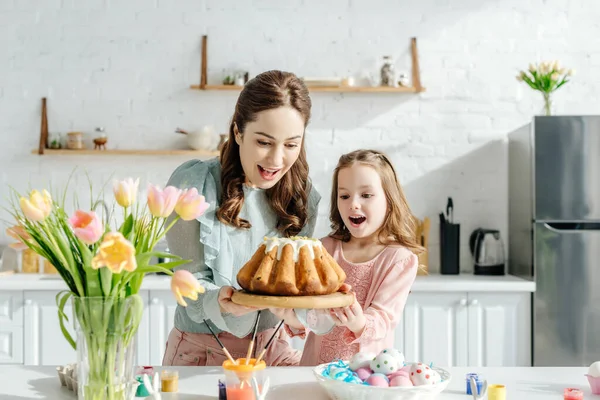 Madre e bambino eccitati guardando il pane pasquale vicino alle uova di Pasqua, conigli decorativi e tulipani — Foto stock