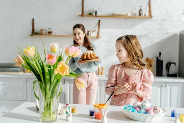 Enfoque selectivo del niño cerca de huevos de pollo y la madre con pastel de Pascua - foto de stock