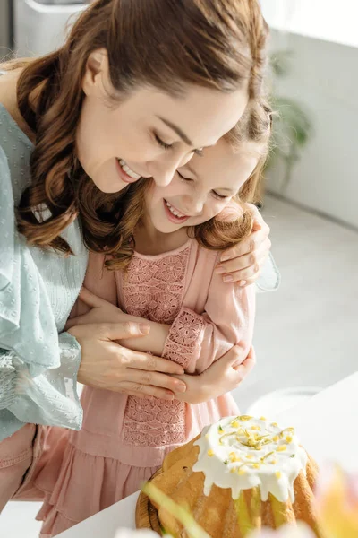 Selective focus of happy woman hugging daughter while looking at easter cake — Stock Photo